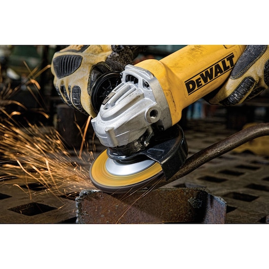 A close-up of a yellow DEWALT angle grinder in use, grinding metal and producing sparks. The person's hand is wearing a protective glove.