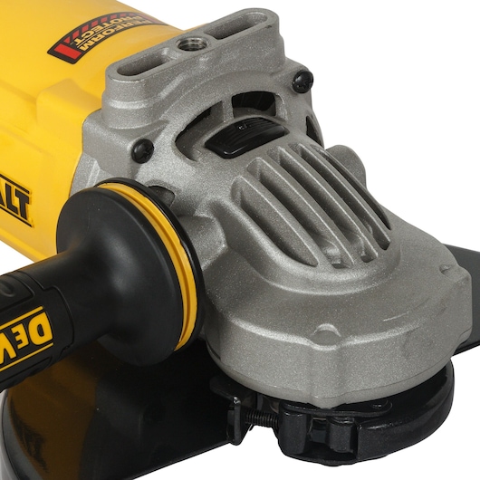 Close-up view of a DEWALT angle grinder, showing its metallic gear housing, black handle with yellow accents, and part of the grinding disc.