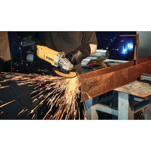 A person wearing gloves using a DEWALT angle grinder to cut a large metal beam, with bright sparks flying from the contact point.