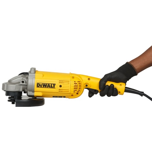 A person wearing a black glove is holding a yellow DEWALT angle grinder, model DWE496, with a power cord attached. The tool is photographed against a white background.