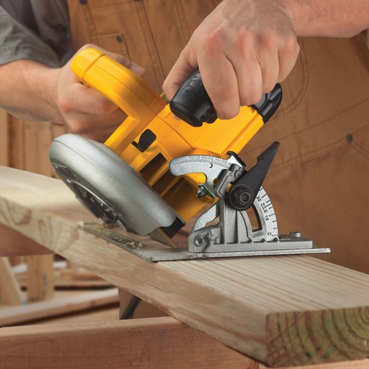 A person using a yellow DEWALT circular saw to cut a piece of wood at an angle, with a close-up view showing the saw and the wood in a workshop setting.