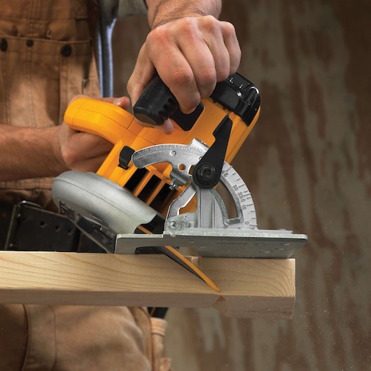 Close-up of a person using a DEWALT circular saw to cut a wooden plank. The saw is yellow and silver with a visible angle adjustment mechanism.