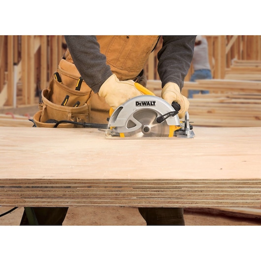 A person using a DEWALT DWE575 circular saw to cut plywood sheets at a construction site. The person is wearing work gloves and a tool belt.