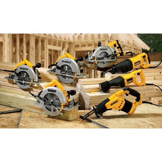Several DEWALT power tools, including circular saws and reciprocating saws, are displayed on stacks of wooden beams at a construction site with a wooden frame structure in the background.