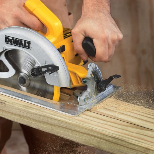 A close-up of a person using a DEWALT circular saw to cut a wooden plank, with sawdust flying from the area being cut.