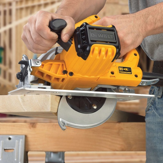 A person is using a DEWALT DWE575 yellow circular saw to cut through a piece of wood in a construction setting.