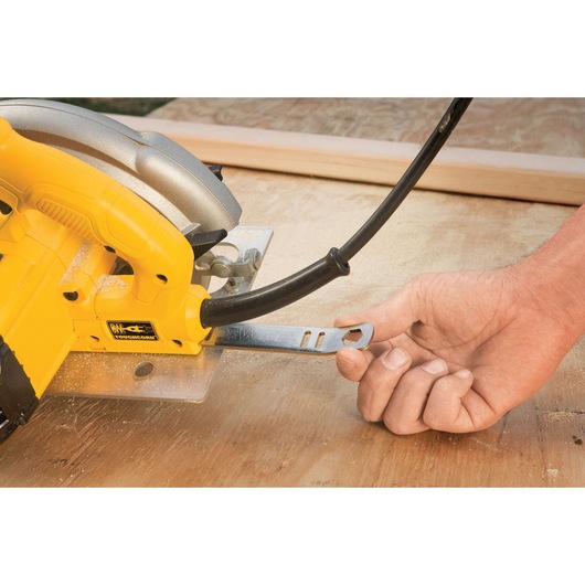 A close-up view of a hand holding a metal wrench attached to a yellow DEWALT circular saw, placed on a wooden surface.