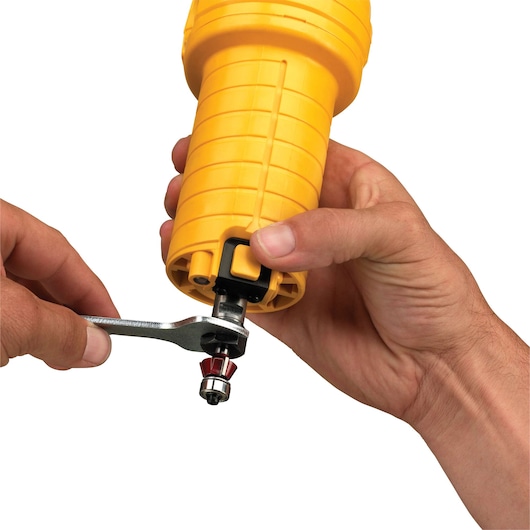 Close-up of hands using a wrench to adjust a bit on a yellow DEWALT power tool.