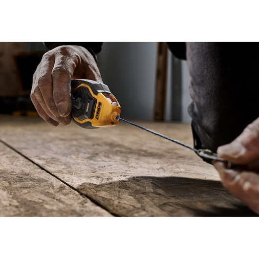 A close-up of a person's hands using a DEWALT chalk line tool on a wooden surface, with the blue chalk line extended for marking.