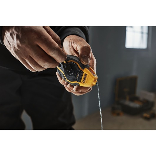 Close-up of a person holding and using a DEWALT chalk line tool, with a yellow and black design, in a workshop setting.