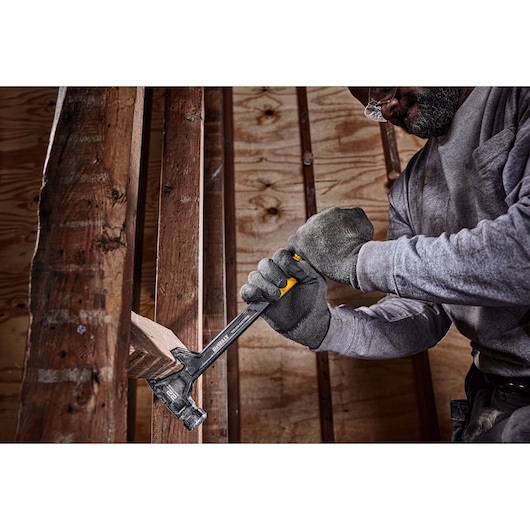 A person wearing gloves is using a DEWALT DWHT51008 hammer to pull a nail from a wooden beam inside a construction site.