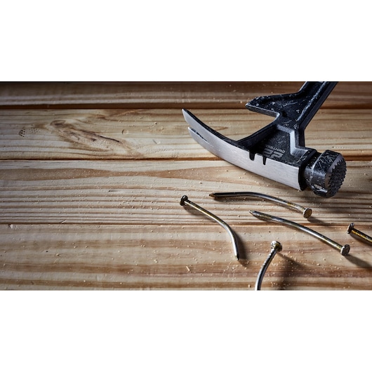 Close-up of a DEWALT claw hammer resting on a wooden surface, with several bent metal nails lying beside it.