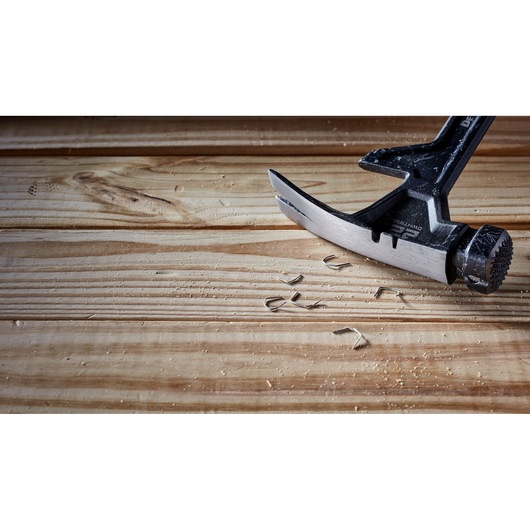 A close-up view of a DEWALT claw hammer resting on a wooden surface with metal nail pieces and wood shavings beside it.