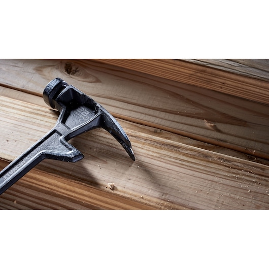 A close-up of a DEWALT claw hammer lying on wooden planks, with some wood shavings visible.