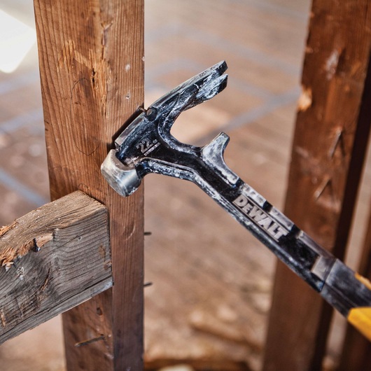 A close-up view of a DEWALT hammer being used on a wooden frame during construction or demolition work.