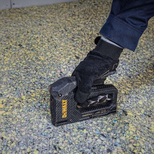 A gloved hand holds a DEWALT carbon fiber stapler (model DWHT80276) against a textured surface, likely for flooring or carpeting installation.