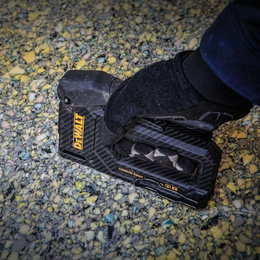 A person wearing a black glove is using a DEWALT carbon fiber hand tool, likely a staple gun, on a textured surface with yellow and multicolored speckles.