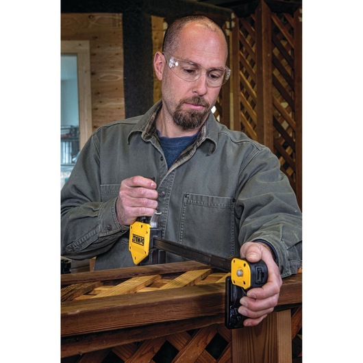 A person with their face blurred is using a DEWALT DWHT83186 woodworking clamp to secure a piece of wood with a lattice pattern, likely during a construction or carpentry project. The clamp is yellow and black and is tightly attached to the wood.