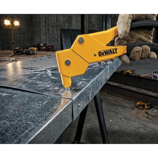 DEWALT rivet tool used on metal sheet in a workshop by a gloved hand. Other tools are visible in the background.