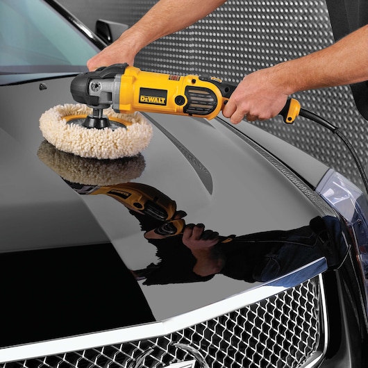 A person using a yellow DeWalt electric buffer to polish the hood of a black car.