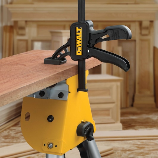 DEWALT clamp secures a wooden plank on a yellow workstation in a workshop setting.