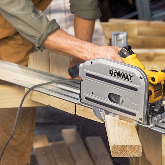 A person using a DEWALT track saw to cut a piece of wood. The saw is positioned on a guide rail for precise cutting in a woodworking setting.