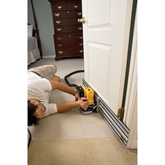 Person using a DEWALT track saw to cut the bottom edge of a white interior door, while the door is installed in a carpeted room.