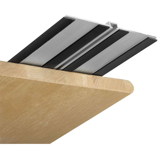 Close-up of a guide rail for a power tool, placed on the edge of a wooden board. The rail features metal and rubber components designed to stabilize and guide cutting equipment.