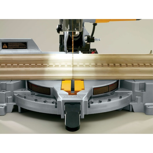 Close-up view of a DEWALT miter saw with its laser guide activated, showing the saw blade aligned with a piece of wood on the cutting platform.