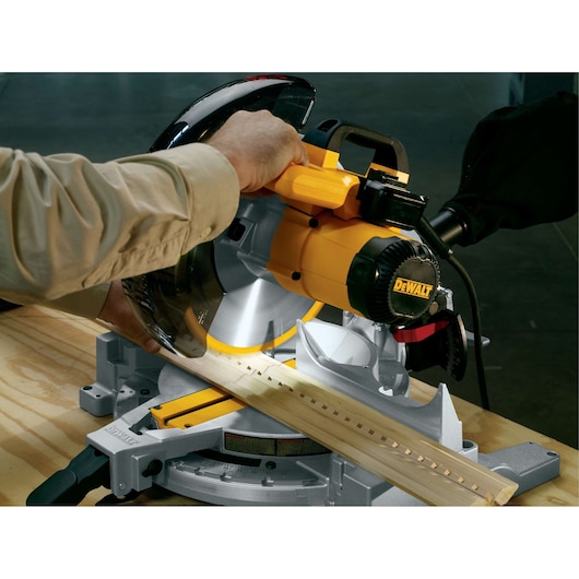 A person using a DEWALT miter saw to cut a piece of wood on a workbench.