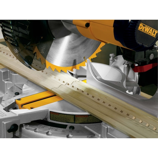 Close-up view of a DEWALT miter saw in operation, cutting a piece of light-colored wood.