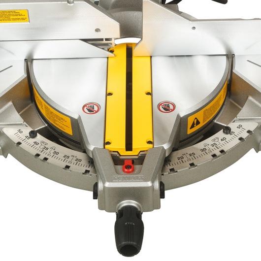 Close-up view of a DEWALT DWS715 miter saw base, showing the angle measurement scale, yellow safety labels, and a yellow blade slot.