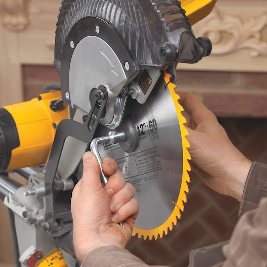 Close-up of a person changing the blade on a DEWALT miter saw, using a wrench to loosen the bolt holding the circular saw blade in place.