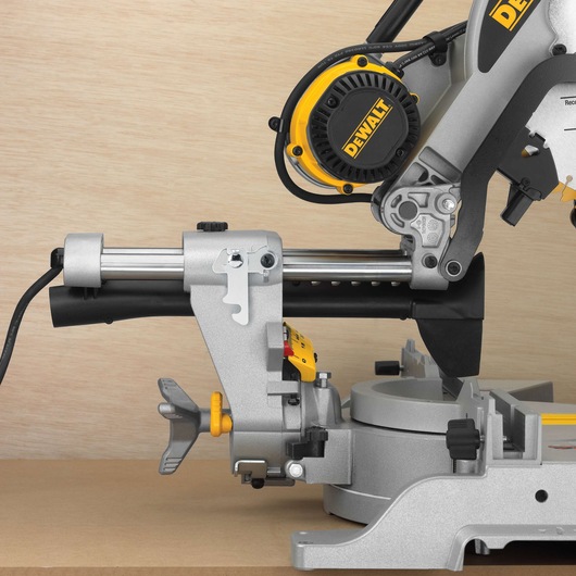 Close-up view of a DEWALT DWS780 sliding compound miter saw placed on a wooden surface, with visible power cord, motor housing, and adjustment knobs.