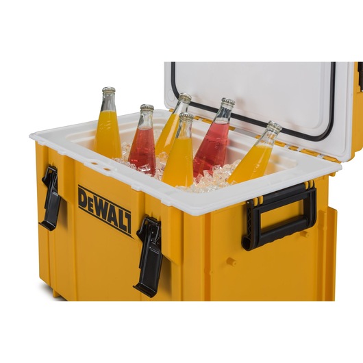 A yellow DEWALT cooler box with its lid open, showing several glass bottles of orange and red drinks placed on ice inside.