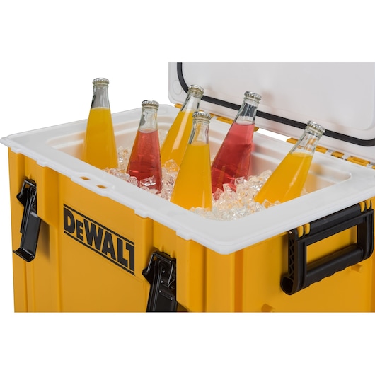 A yellow DEWALT cooler box with the lid open, containing ice and several glass bottles with orange and red beverages.