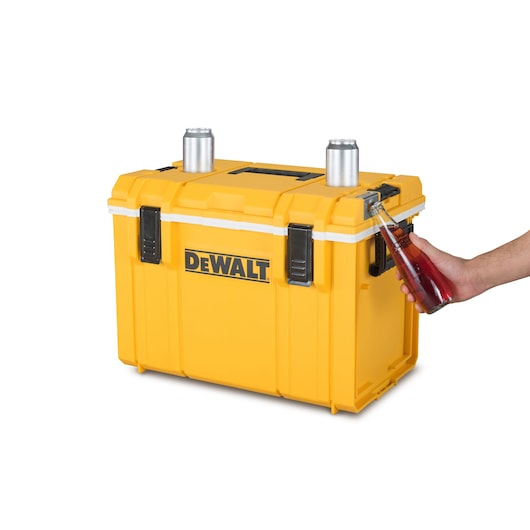 Yellow DEWALT cooler box with cans on top and a person using the built-in bottle opener on the side.