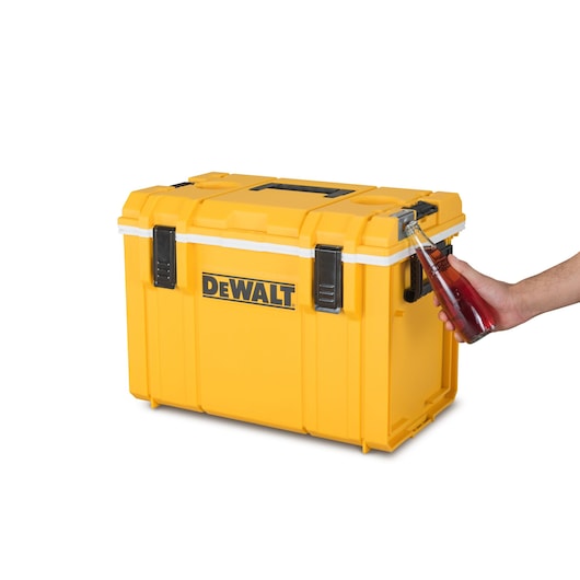 A yellow DEWALT storage box with black clasps, being used as a bottle opener by a hand holding a glass bottle.