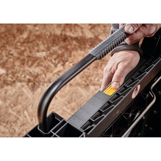 Close-up of a person's hand operating the handle and latch of a DEWALT plastic toolbox, shown on a wood surface.