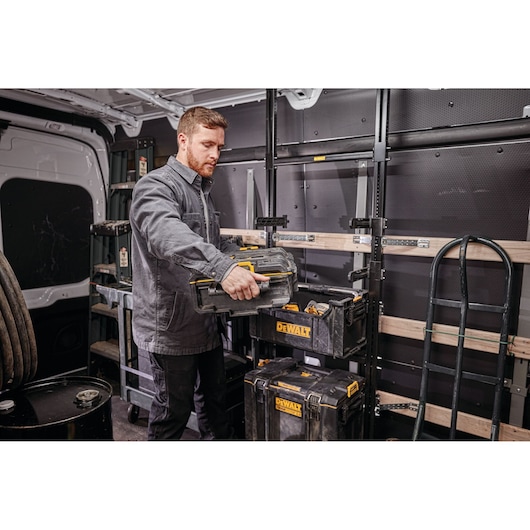 Person organizing DEWALT toolboxes inside a work van with shelves and equipment visible in the background.
