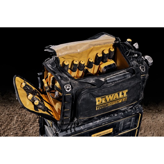 A DEWALT TOUGHSYSTEM 2.0 black and yellow tool bag is open, showing the interior filled with hand tools organized in pockets. The bag is sitting on top of a matching storage box and is suitable for carrying and organizing tools.