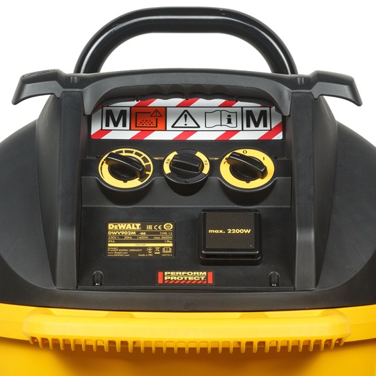 Close-up view of the control panel of a DEWALT DWV902M-QS industrial vacuum cleaner. The panel features three black and yellow adjustment knobs, safety warning labels including icons for medium dust class (M), a caution sign, and operating instructions, along with product specifications such as max 2200W and Perform Protect branding.