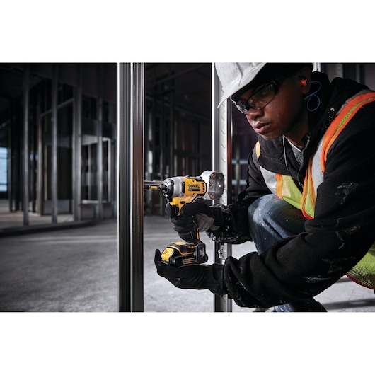 ATOMIC brushless cordless compact impact driver being used by person on a metallic beam.