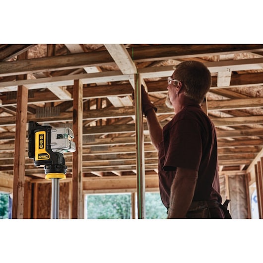 3 line green laser level mounted on a tripod and being used by a construction worker.